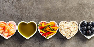 Healthy cooking ingredients placed in long straight row of small heart-shaped bowls, studio shot from above over grey background cropped in wide frame for banner. Organic food concept